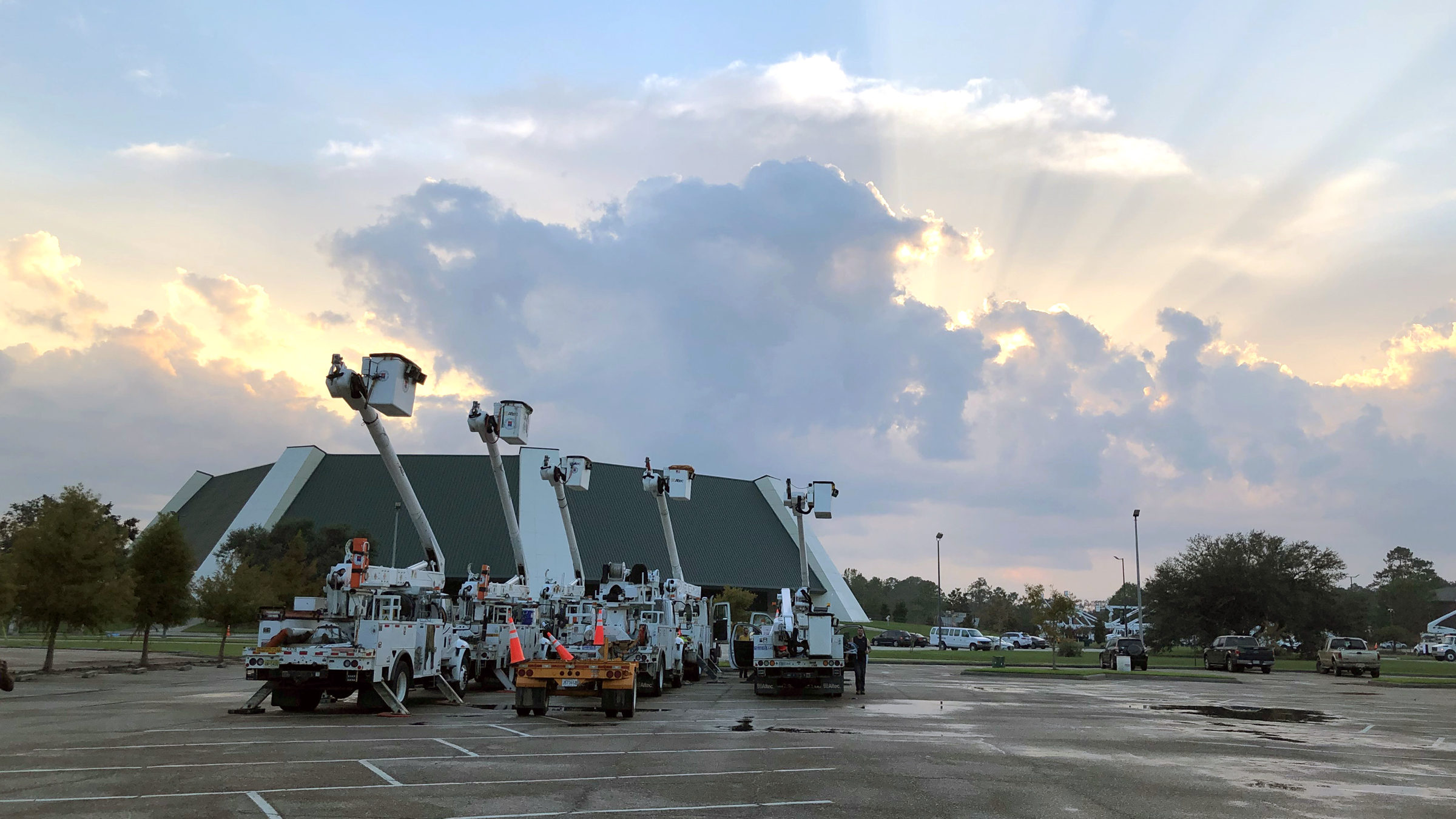 The sun shines behind clouds overlooking the University Center and bucket trucks at Southeastern in Hammond, Louisiana. 